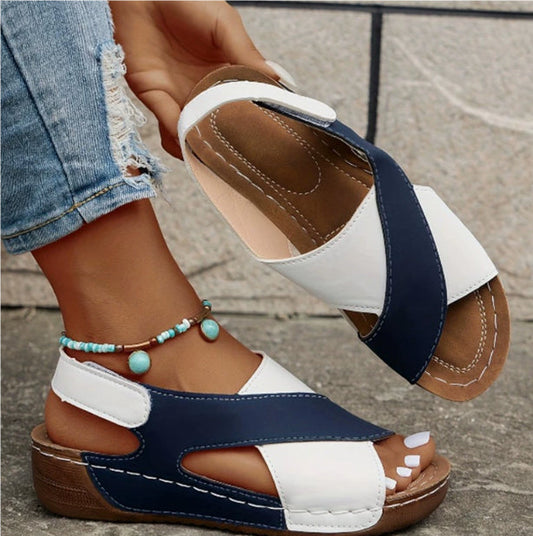 Pair of multicolored sandals worn with denim jeans on a stone pavement background