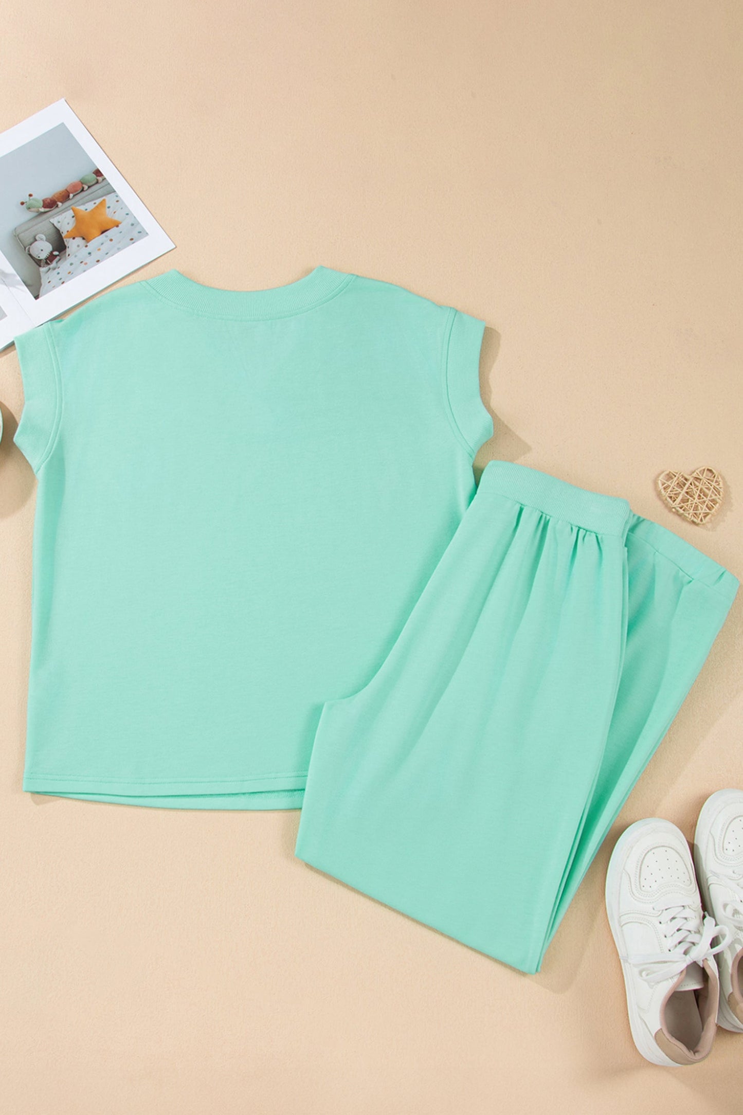 Light green sleeveless top and shorts set on a beige surface with a magazine and heart-shaped object.