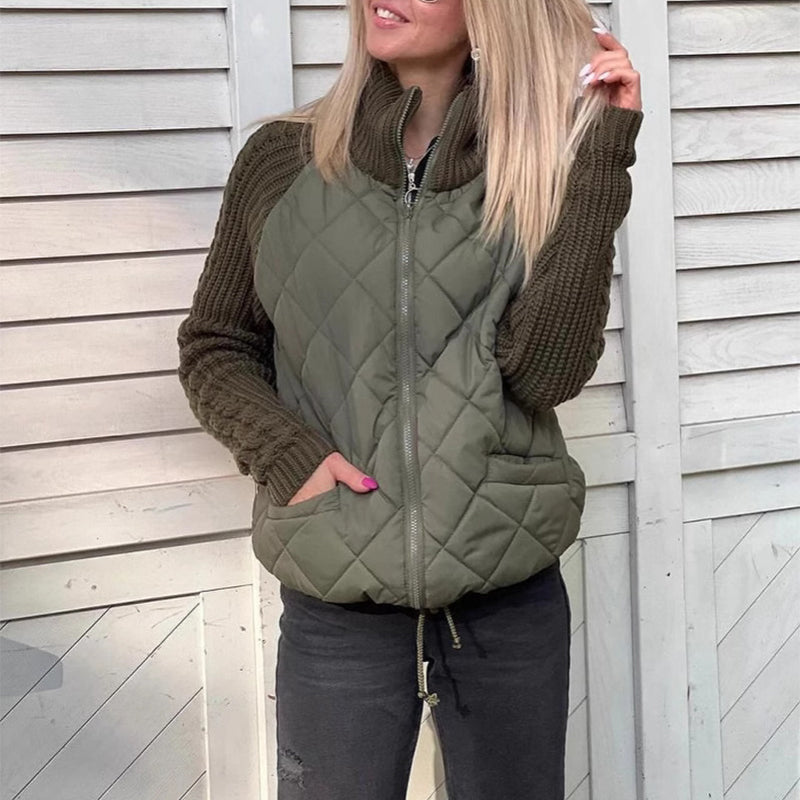 Woman wearing a green quilted vest over a brown sweater against a wooden wall.
