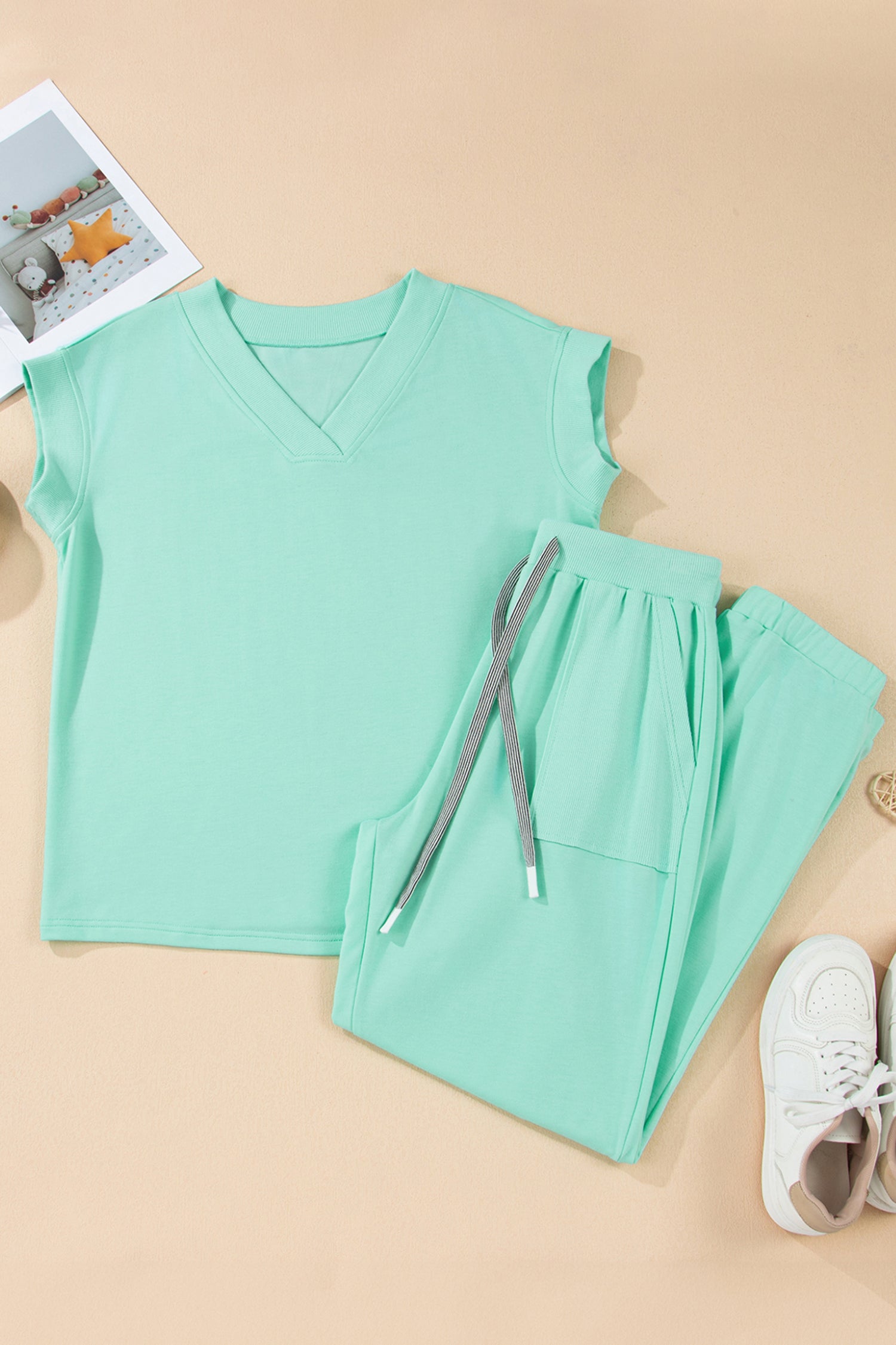 Mint green sleeveless top and pants with a white sneaker on a beige background