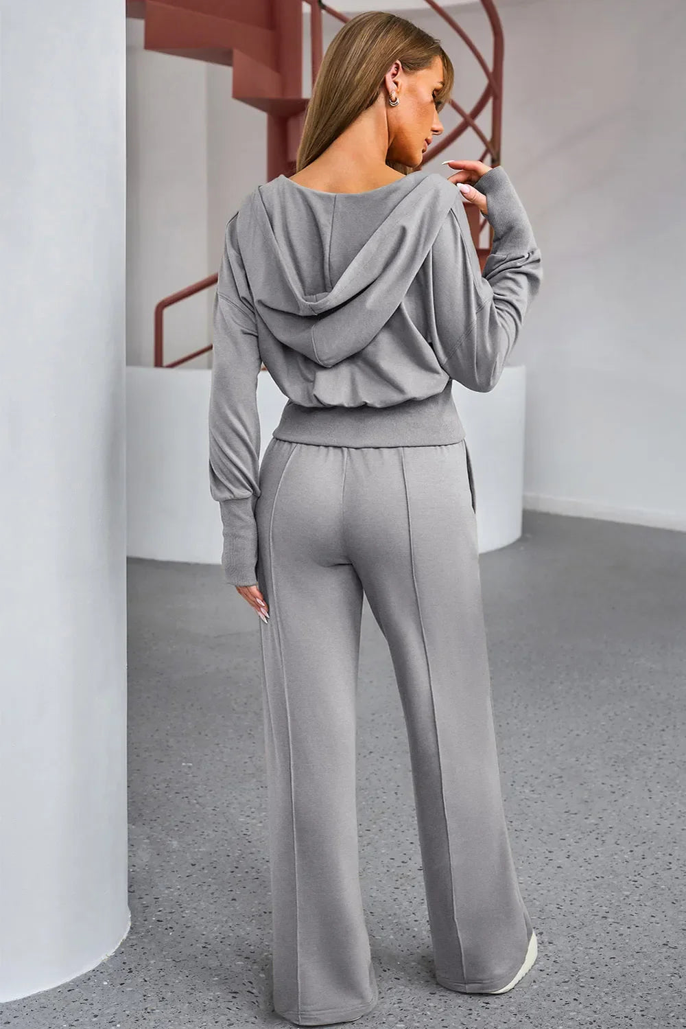 Woman wearing a gray tracksuit in an indoor setting show the back 