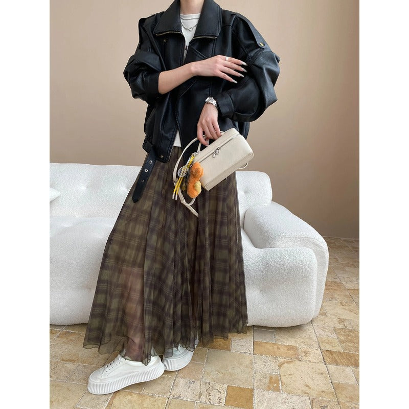 Person wearing a black jacket, plaid skirt, and white sneakers holding a beige handbag.