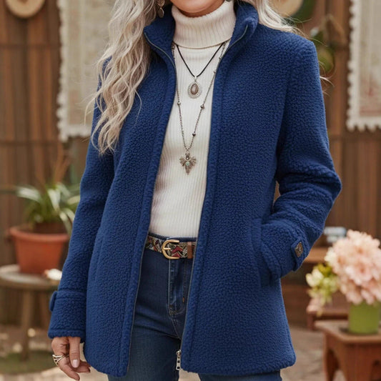 Person wearing a blue coat with a white turtleneck sweater and floral arrangement in the background