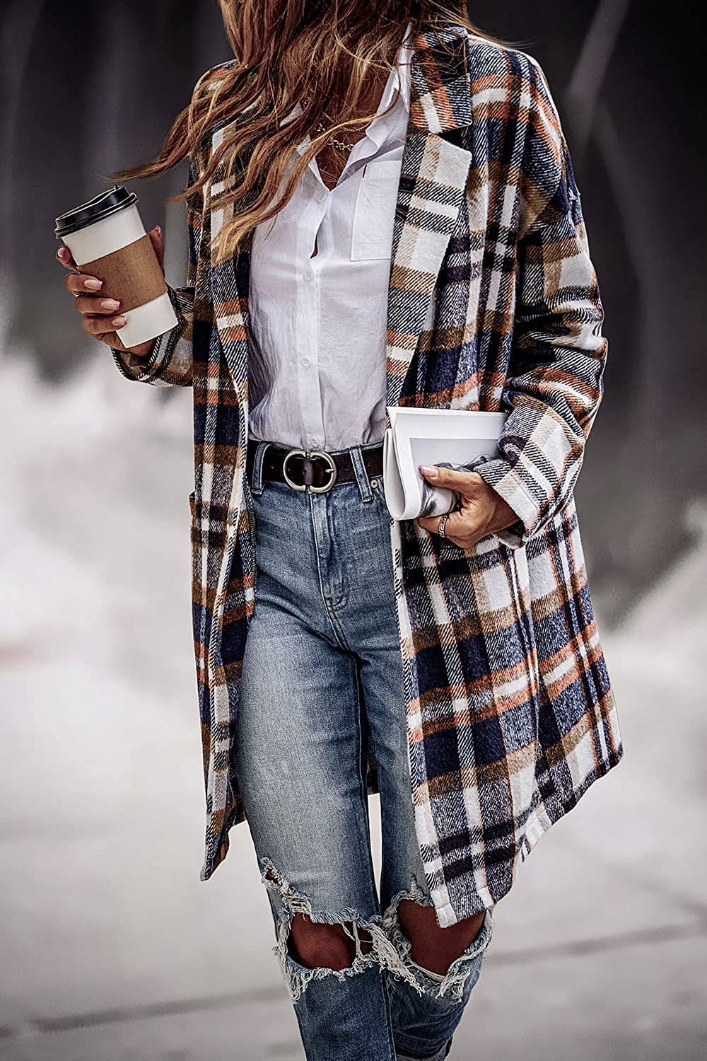 Person wearing a plaid coat over a white shirt and jeans, holding a coffee cup and phone.
