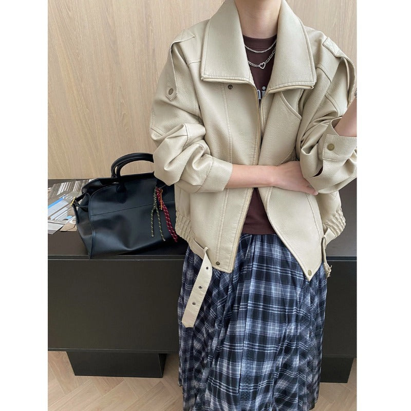 Person wearing a beige jacket and plaid pants with a black bag on a wooden floor.