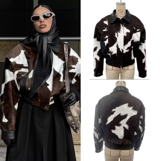 A cropped cow-print jacket shown on a mannequin and worn by a model. The jacket features a brown and white cowhide pattern with black leather trim at the collar, cuffs, and pockets.