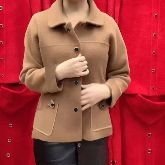 A person wearing a camel brown wool-blend jacket with dark buttons, standing in front of a bright red textured fabric backdrop.