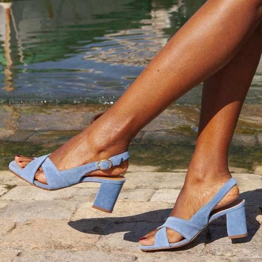A person wearing light blue slingback block-heel sandals with open toes, photographed outdoors near a stone poolside setting.