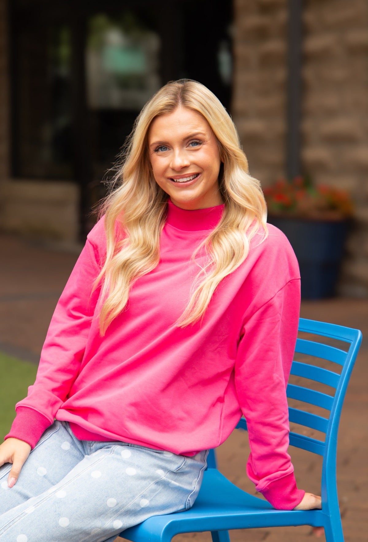 Woman wearing a bright pink sweatshirt sitting on a blue chair outdoors.