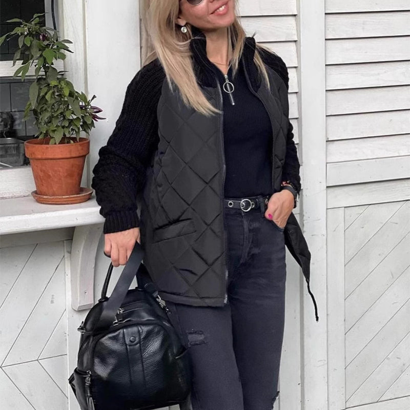 Woman wearing a black quilted vest and carrying a black bag, standing in front of a white wooden door.
