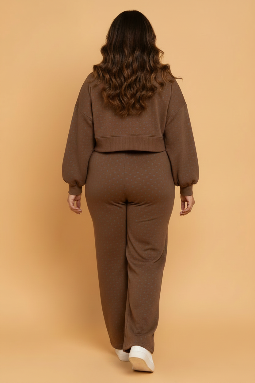 A woman viewed from behind wearing a matching brown knit lounge set with a cropped long-sleeve top and wide-leg pants, standing against a solid warm beige studio background.