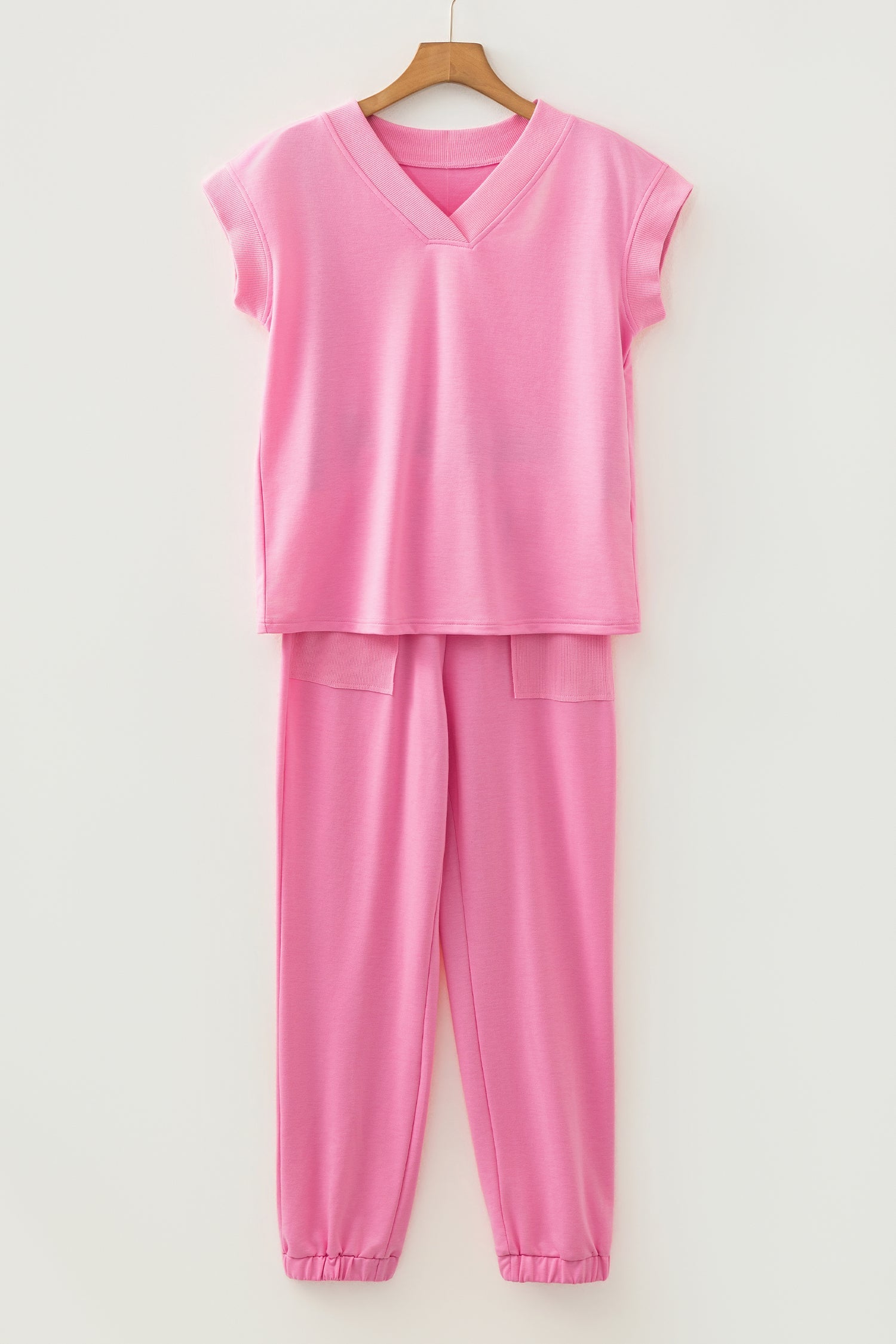 Pink outfit with a top and pants on a hanger against a white background