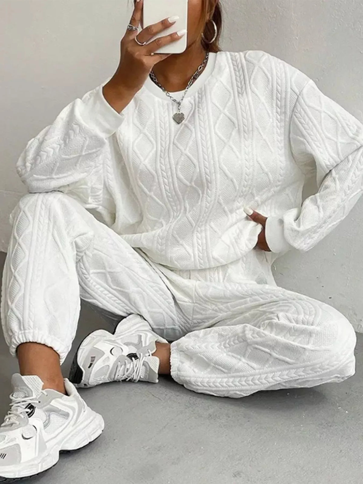 Person wearing a white cable knit tracksuit with sneakers on a gray background