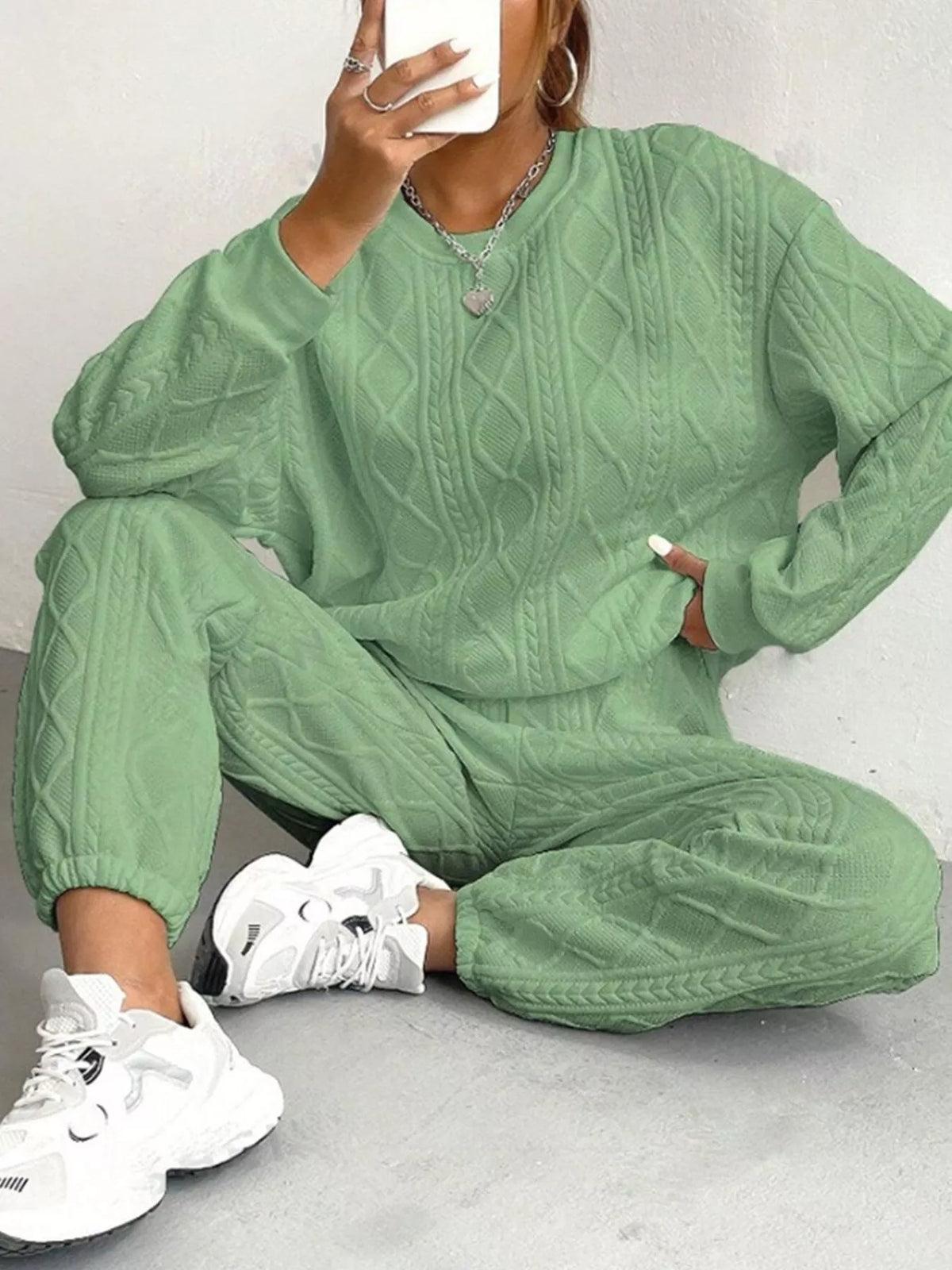 Person wearing a green cable knit outfit with white sneakers on a light gray background