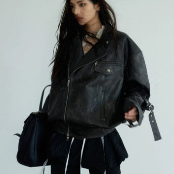 Person wearing a black leather jacket holding a black bag against a plain background