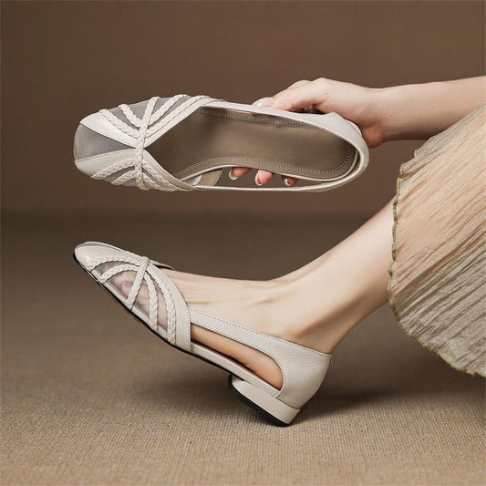 A pair of women's low-heel flat shoes in a light beige or off-white color, shown worn on one foot and held in a hand against a neutral brown studio background.