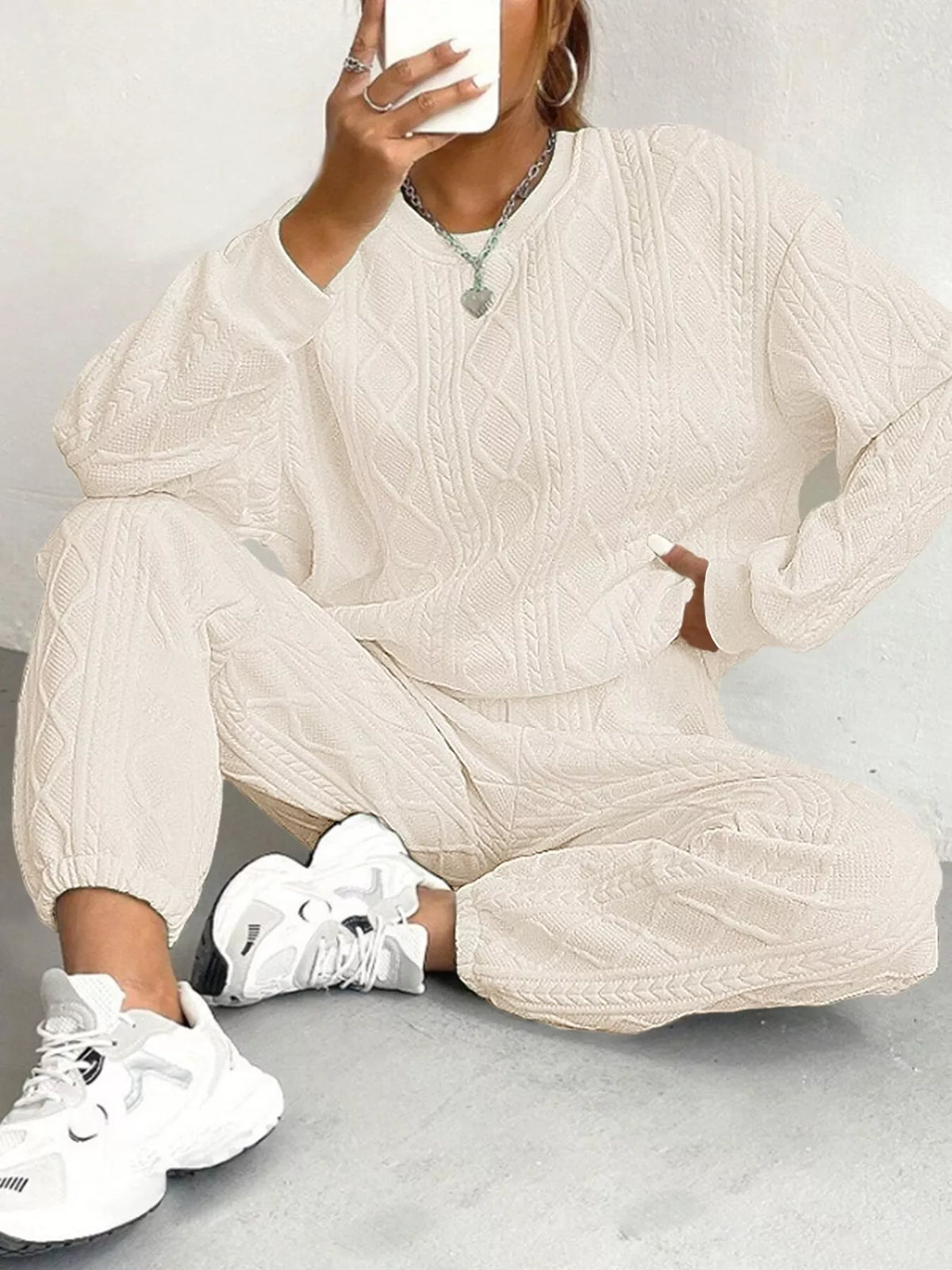 Person wearing a beige cable knit outfit with white sneakers on a light gray background