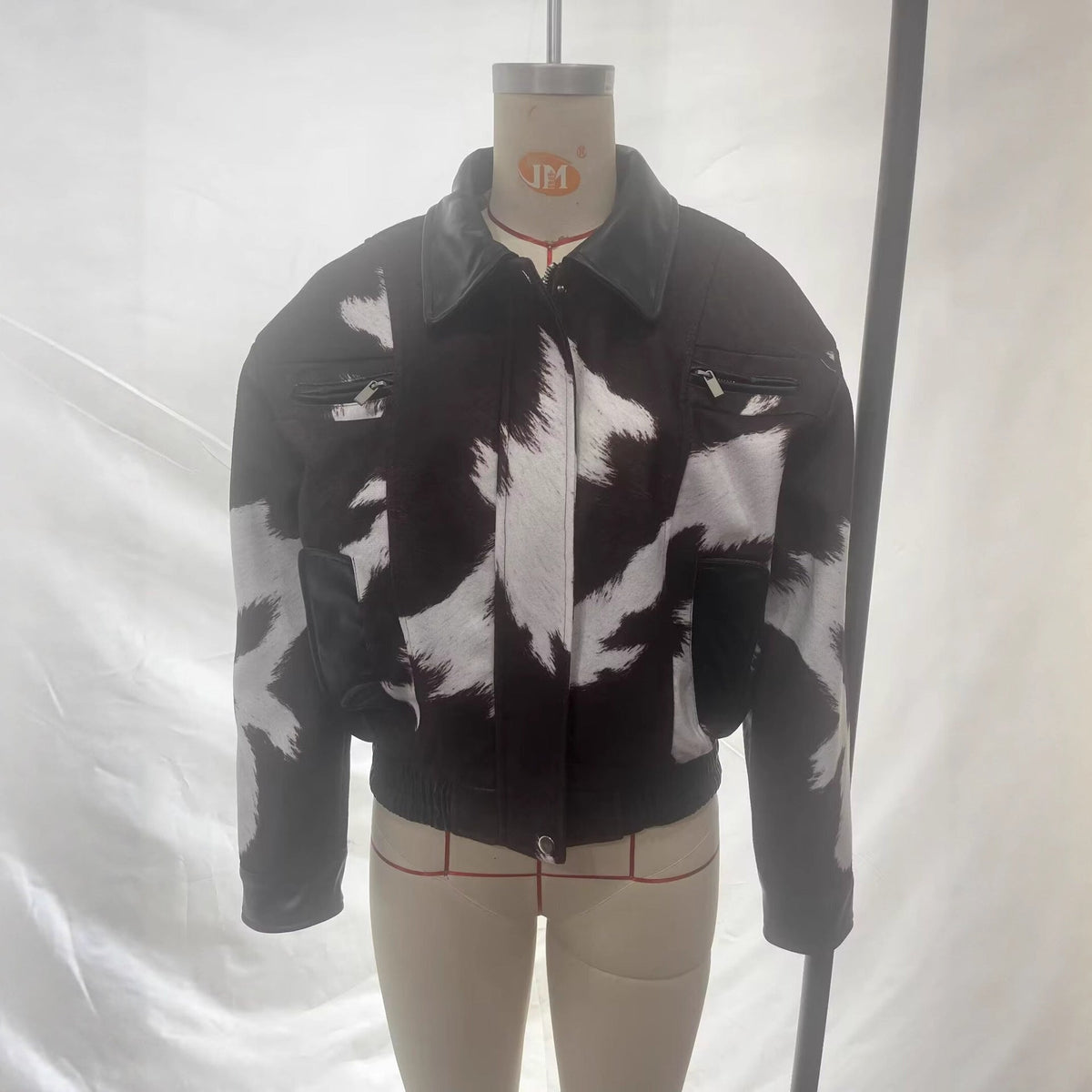A black and white cow-print jacket displayed on a beige mannequin torso against a white fabric backdrop.