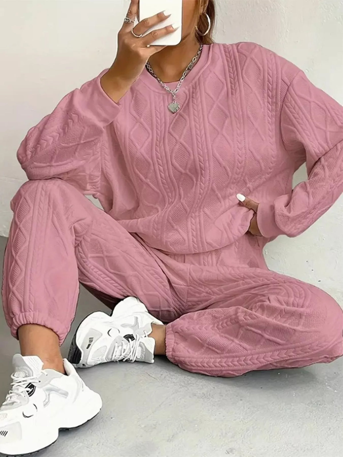 Person wearing a pink textured tracksuit with white sneakers on a light background